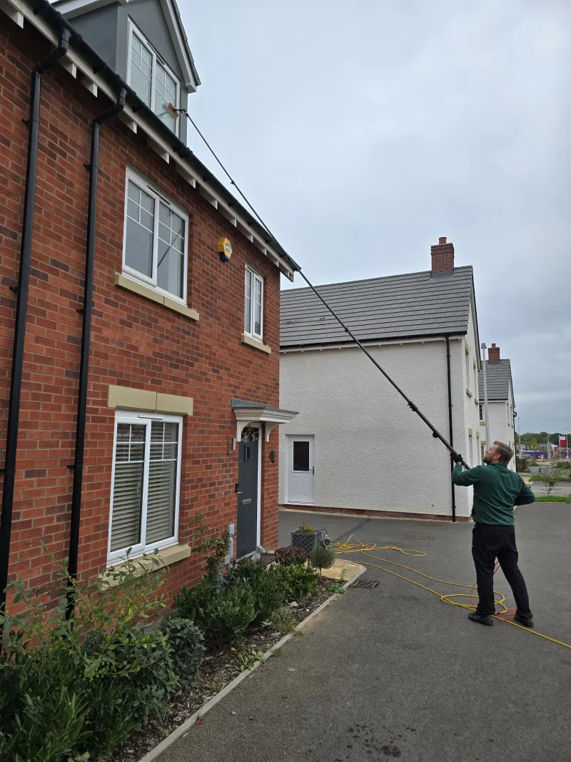AZP Wash cleaning the dormer window of a red-brick house with a water-fed pole, working from the driveway